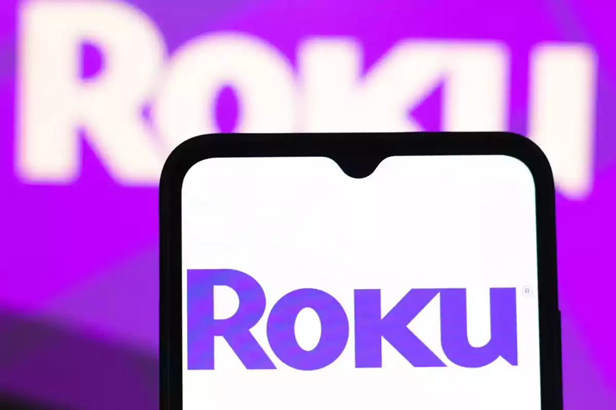 Roku logo on a mobile phone screen with a blurred purple-toned background Roku logo on a mobile phone screen with a blurred purple-toned background