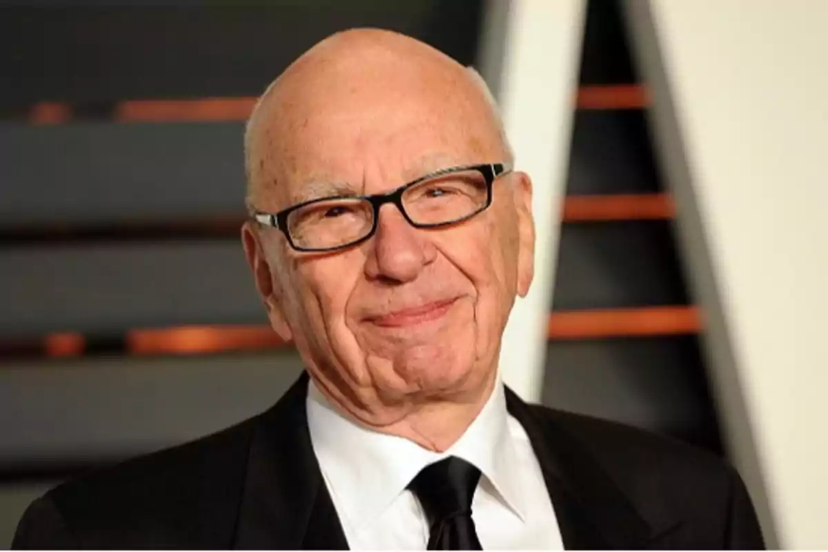 Bald older man with glasses and a dark suit smiles slightly in front of a blurred background Bald older man with glasses and a dark suit smiles slightly in front of a blurred background