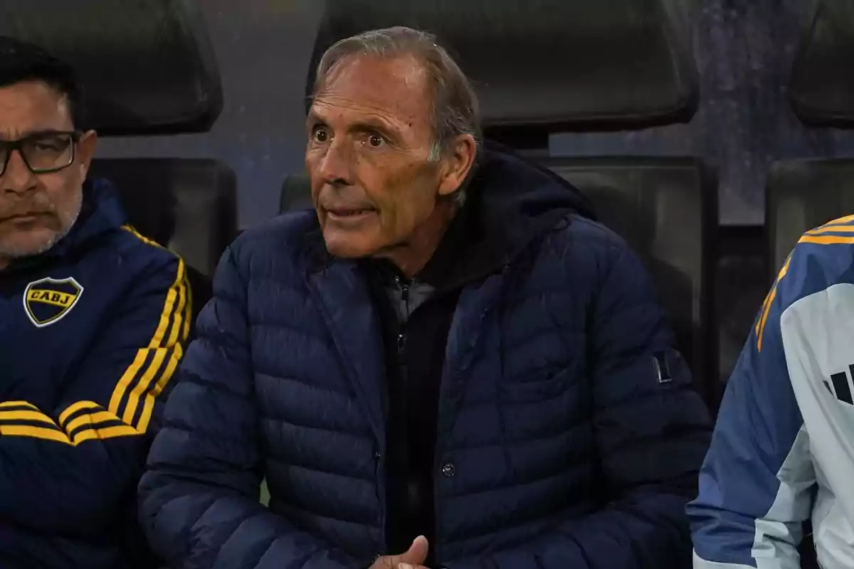 Older man in a blue jacket sitting on the bench next to other people wearing Boca Juniors sportswear Older man in a blue jacket sitting on the bench next to other people wearing Boca Juniors sportswear