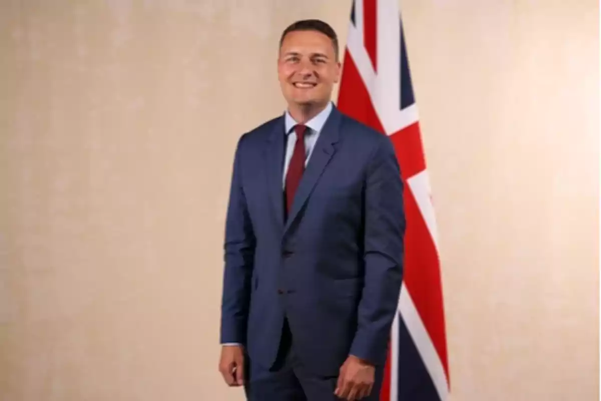 Man in a blue suit posing in front of a United Kingdom flag against a light background Man in a blue suit posing in front of a United Kingdom flag against a light background