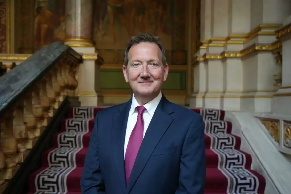 Man in a blue suit and red tie posing on an elegant staircase with a red carpet and gold details Man in a blue suit and red tie posing on an elegant staircase with a red carpet and gold details
