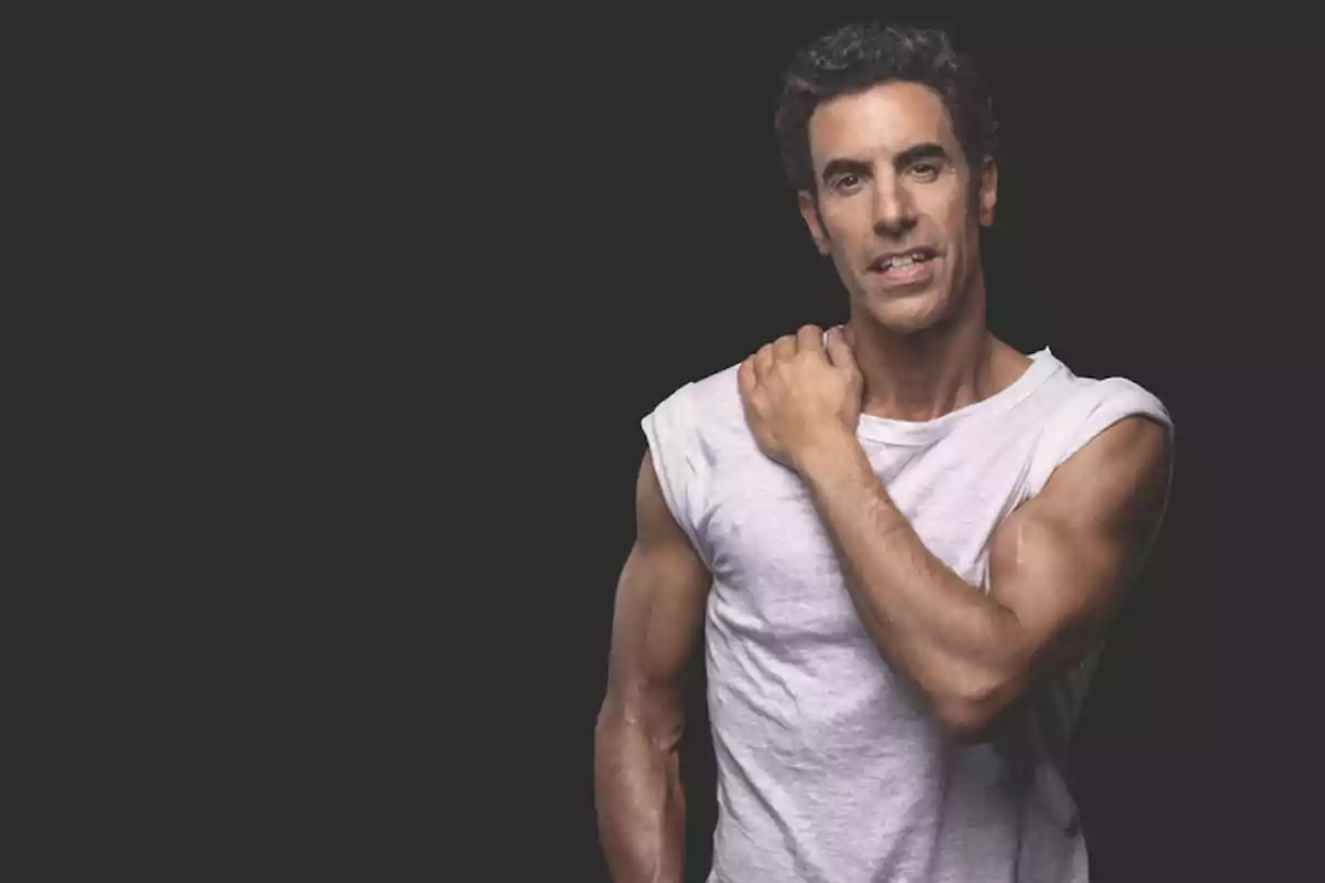 Hombre de cabello rizado y oscuro con camiseta blanca sin mangas posando frente a un fondo negro Hombre de cabello rizado y oscuro con camiseta blanca sin mangas posando frente a un fondo negro