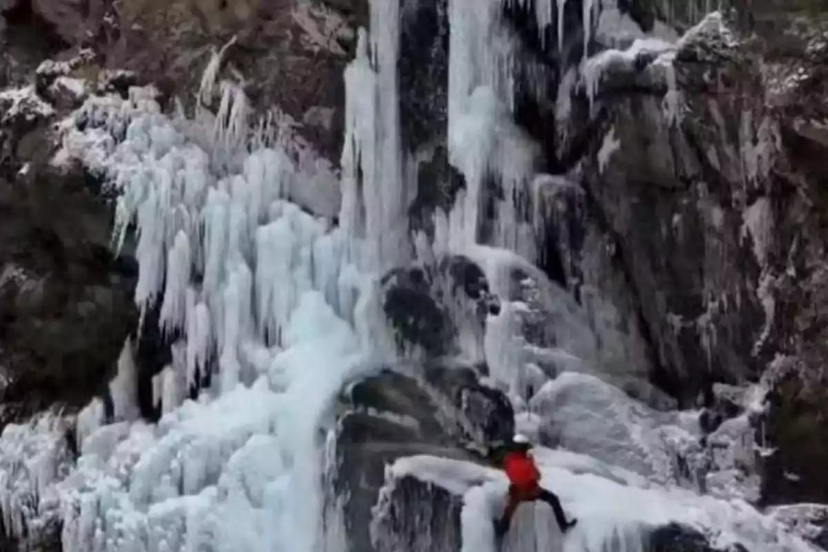 Person climbing a completely frozen waterfall surrounded by ice formations and rocks. Person climbing a completely frozen waterfall surrounded by ice formations and rocks.