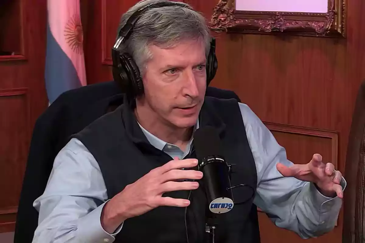 Hombre de cabello canoso usando auriculares y hablando frente a un micrófono en un estudio de radio con una bandera argentina de fondo Hombre de cabello canoso usando auriculares y hablando frente a un micrófono en un estudio de radio con una bandera argentina de fondo