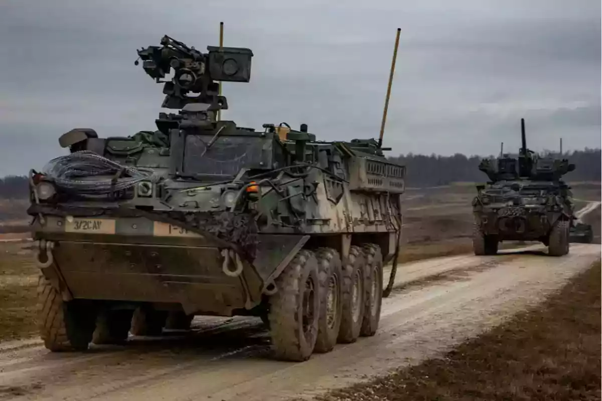 Advanced military armored vehicles move along a dirt road in a rural landscape under a cloudy sky. Advanced military armored vehicles move along a dirt road in a rural landscape under a cloudy sky.