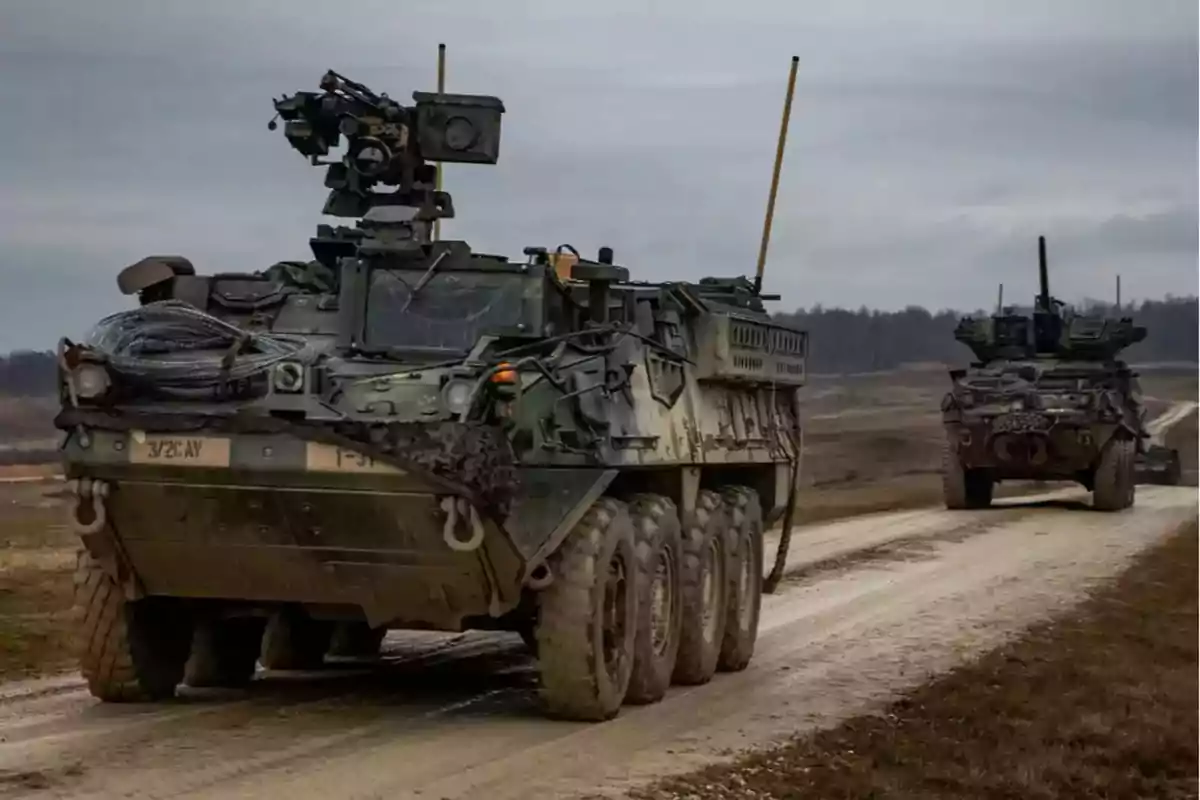 Vehículos blindados militares avanzan por un camino de tierra en un paisaje rural bajo un cielo nublado Vehículos blindados militares avanzan por un camino de tierra en un paisaje rural bajo un cielo nublado