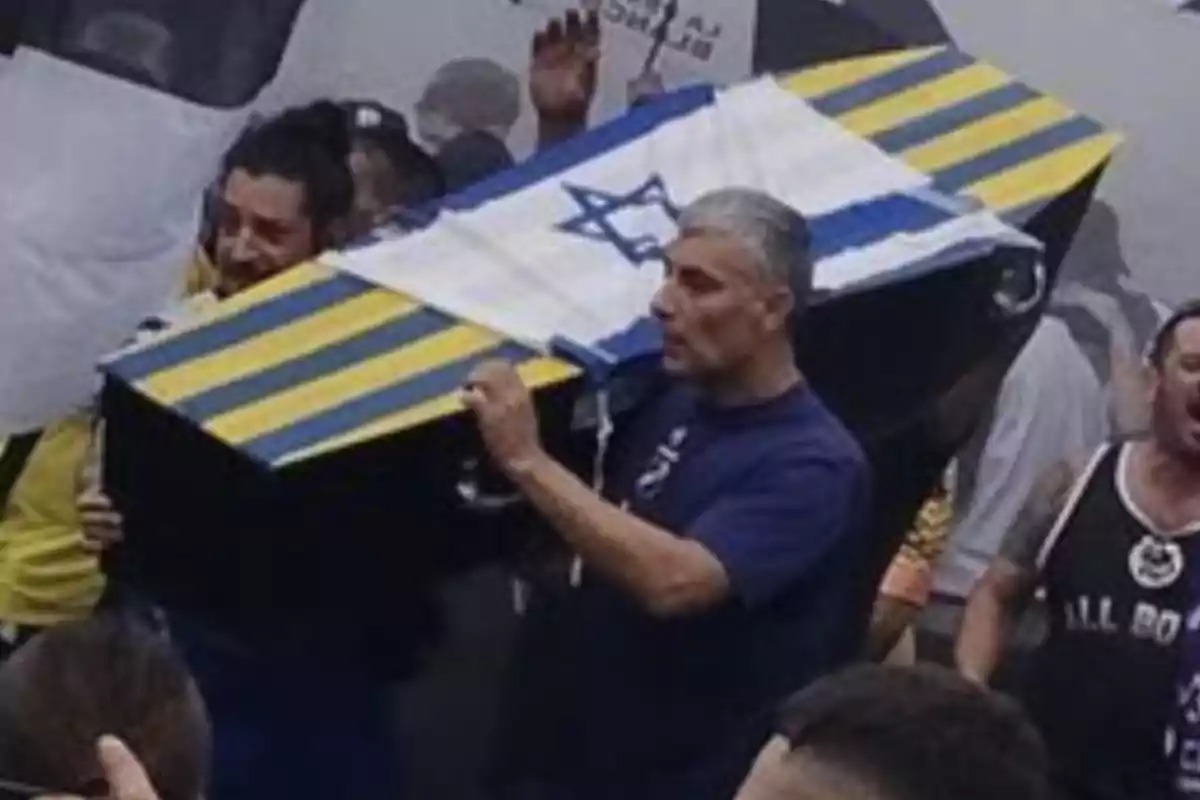 Personas cargando un ataúd decorado con una bandera de Israel y franjas amarillas y azules en medio de una multitud Personas cargando un ataúd decorado con una bandera de Israel y franjas amarillas y azules en medio de una multitud