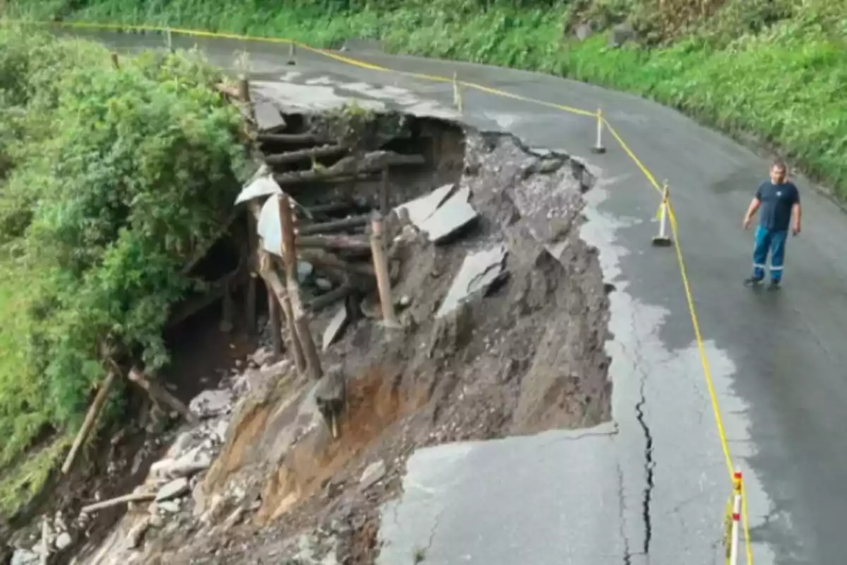 Carretera parcialmente colapsada por un deslizamiento de tierra con un hombre observando la zona acordonada