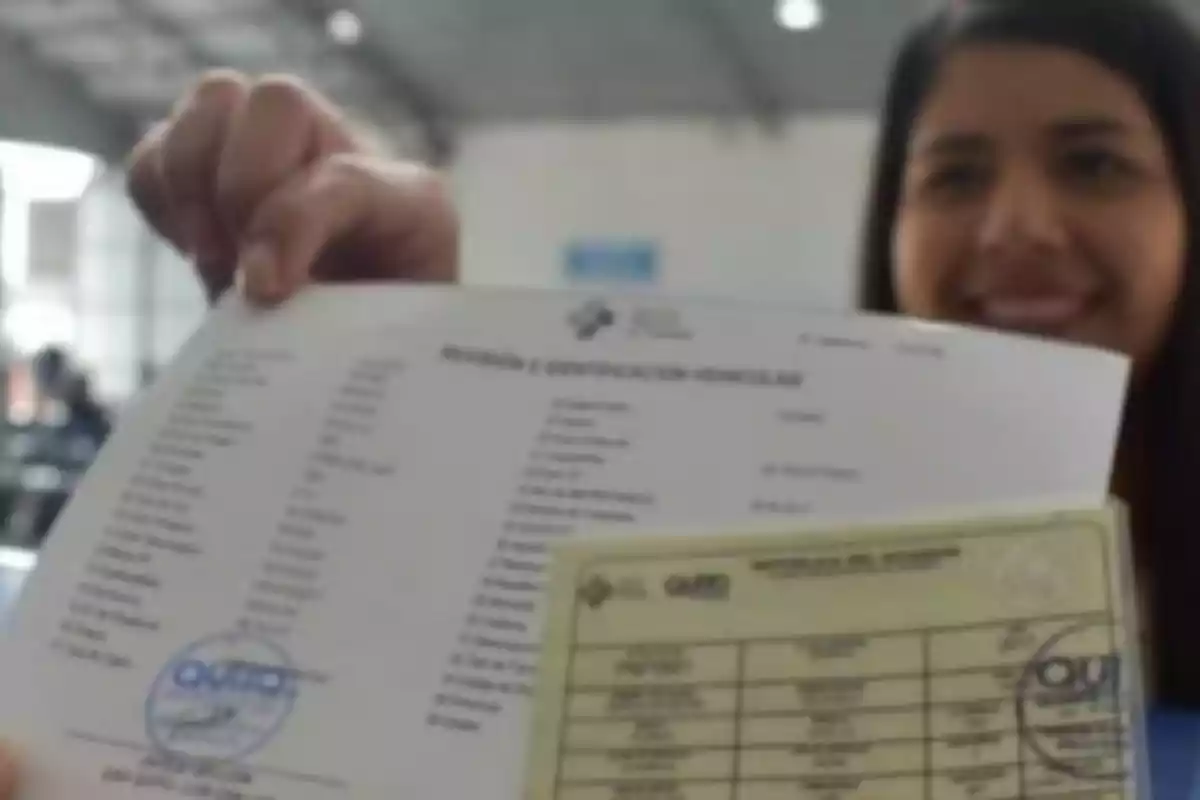 Una persona sostiene documentos oficiales con sellos en un entorno interior, mostrando una sonrisa.
