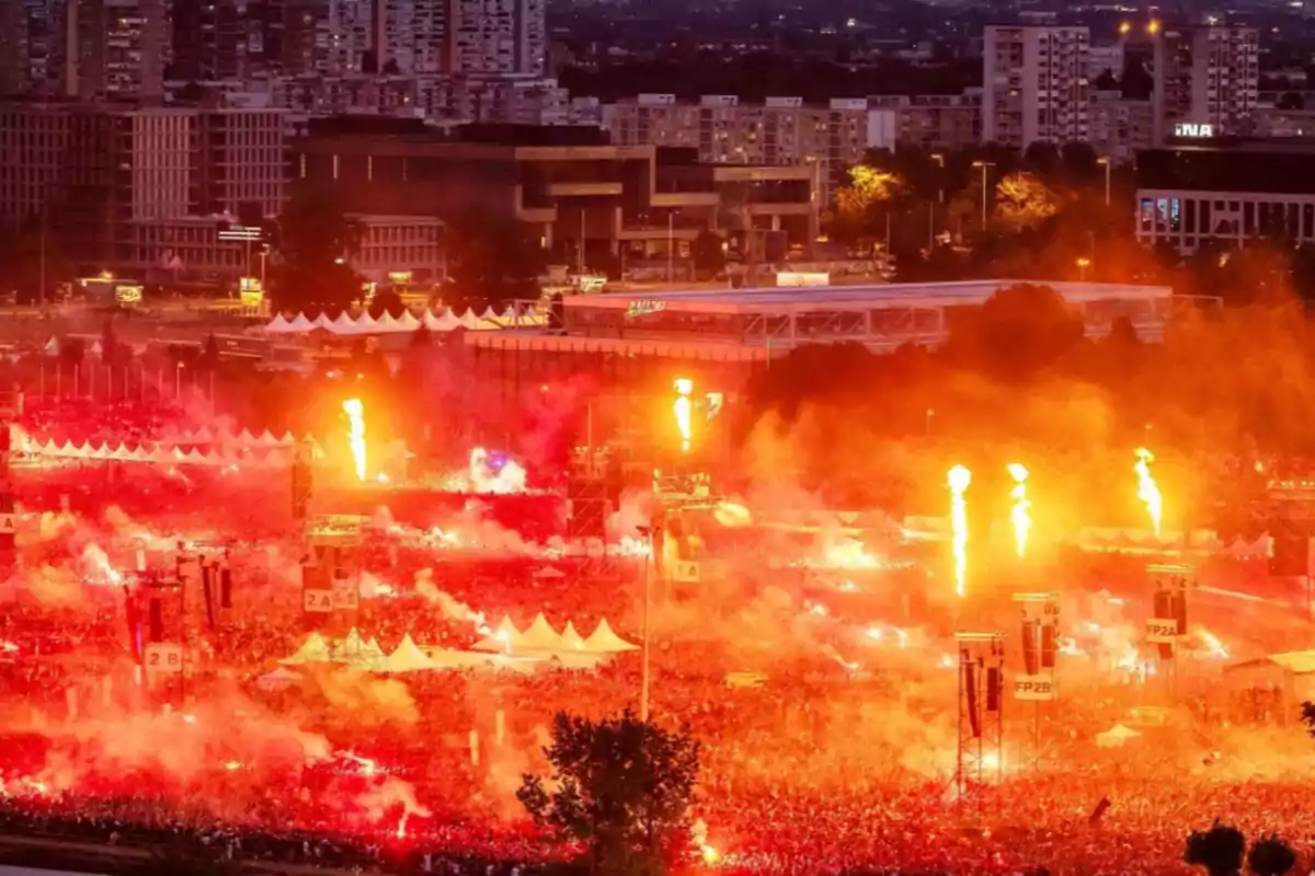 Crowd of people gathered at an outdoor festival with fireworks and red lights illuminating the atmosphere in the city at sunset