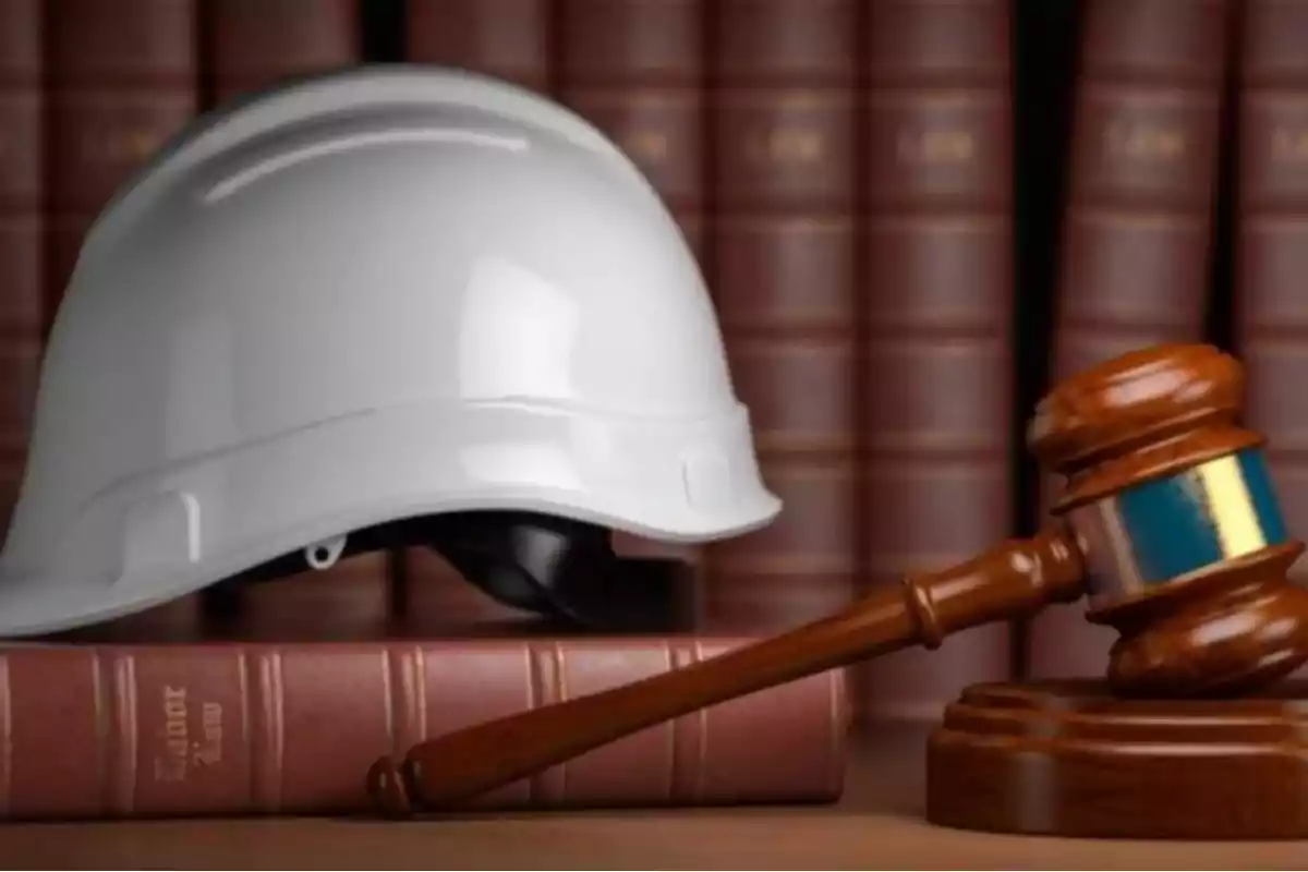A white safety helmet and a judge's gavel on a book with a bookshelf in the background A white safety helmet and a judge's gavel on a book with a bookshelf in the background
