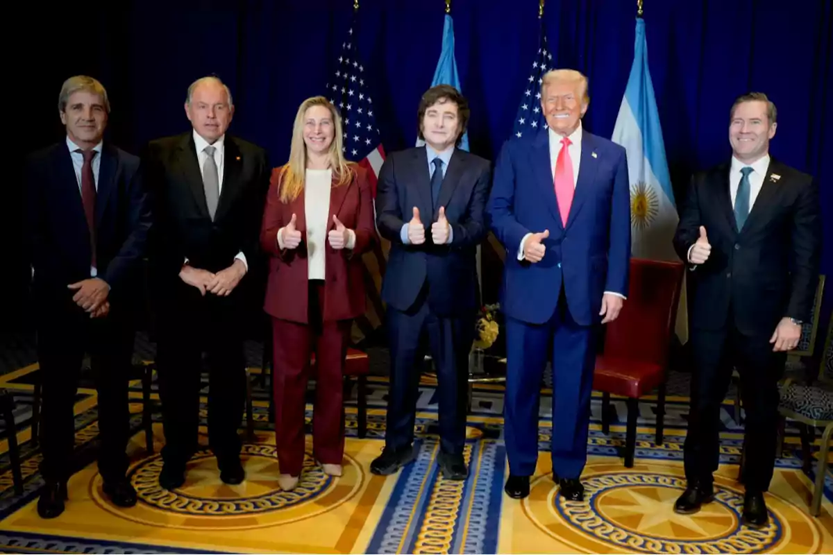 Six people pose for a formal photo in a carpeted room with decorated carpet and United States and Argentine flags in the background; five of them are giving a thumbs up. Six people pose for a formal photo in a carpeted room with decorated carpet and United States and Argentine flags in the background; five of them are giving a thumbs up.