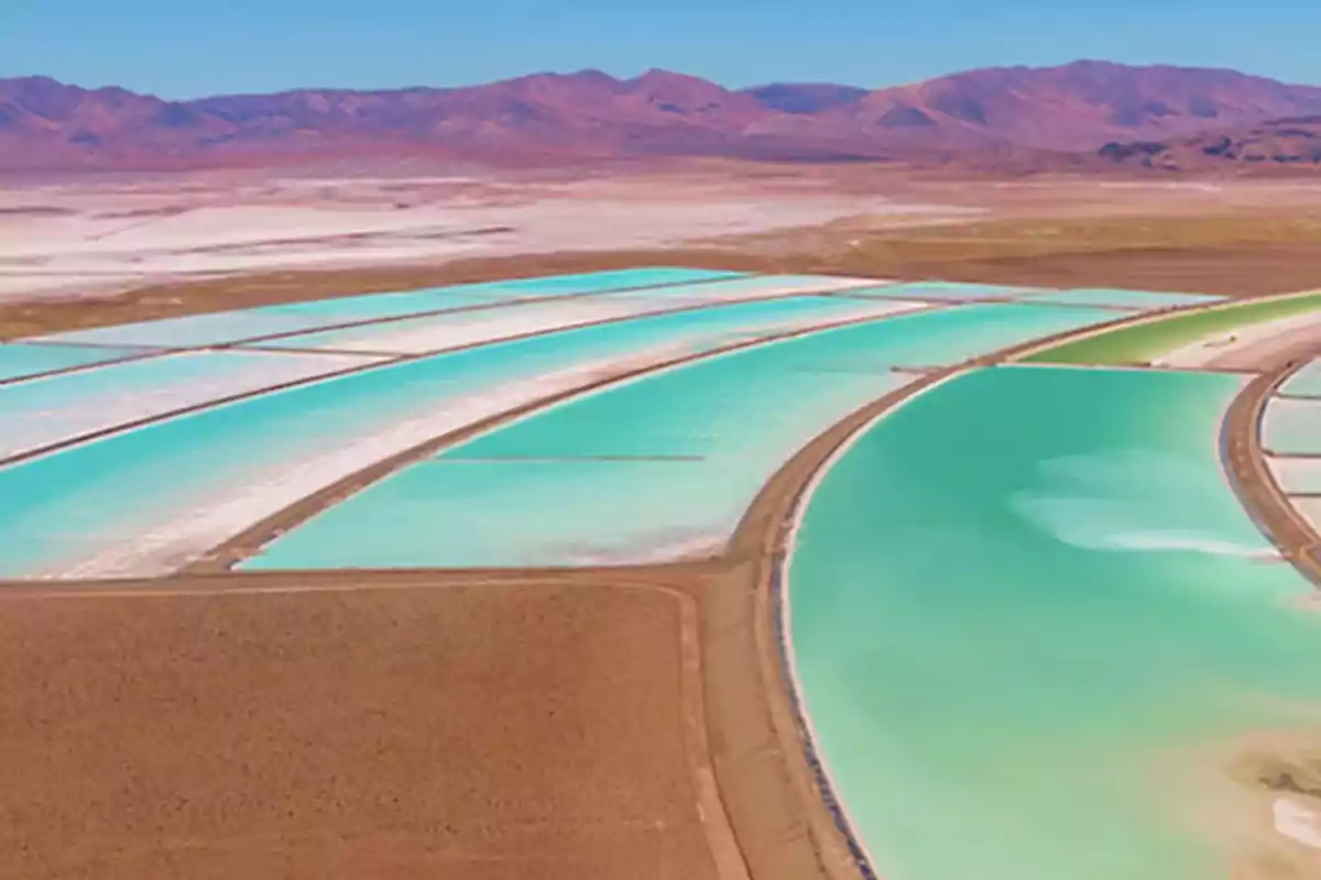 Piscinas de evaporación de agua con tonos turquesa en un paisaje desértico con montañas al fondo