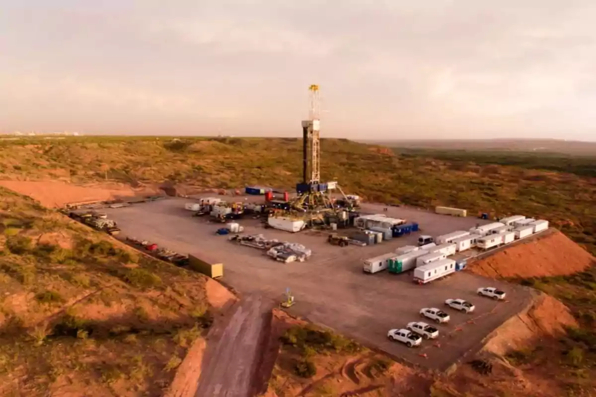Vista aérea de un campo petrolero con una torre de perforación rodeada de vehículos, contenedores y oficinas móviles en una zona desértica Vista aérea de un campo petrolero con una torre de perforación rodeada de vehículos, contenedores y oficinas móviles en una zona desértica
