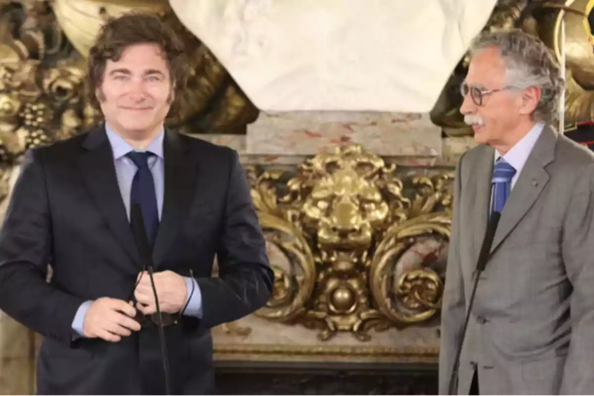 Two men in suits talk and smile in an elegant setting with gold and marble decor.