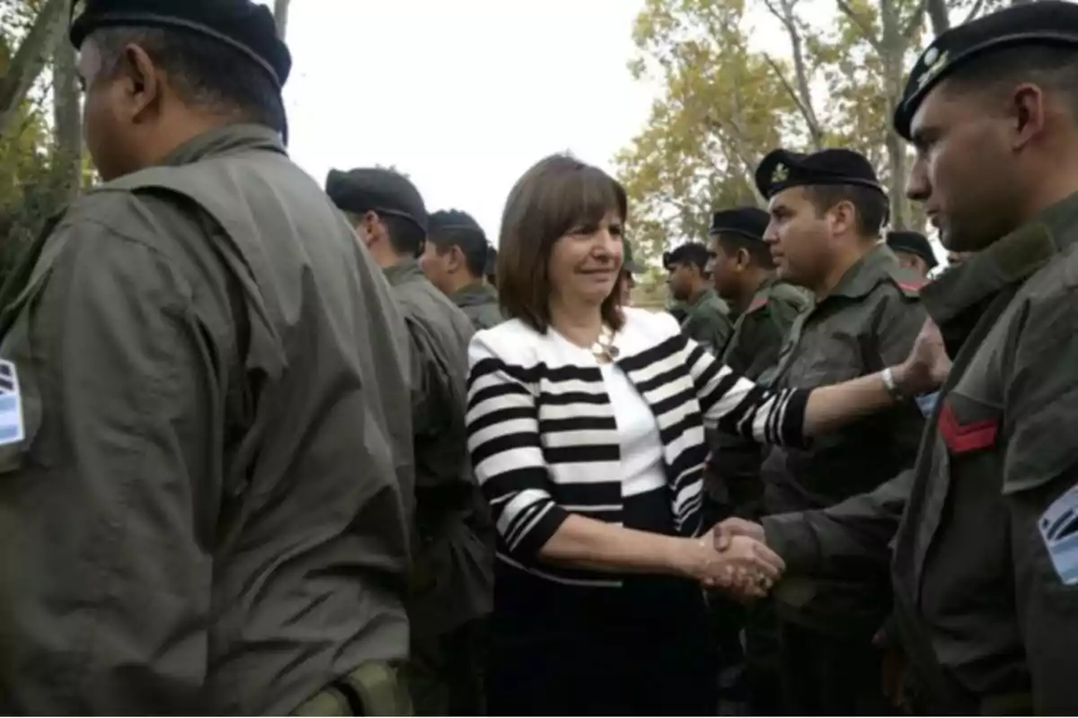 Una mujer con chaqueta a rayas blancas y negras saluda y estrecha la mano de un grupo de hombres uniformados al aire libre
