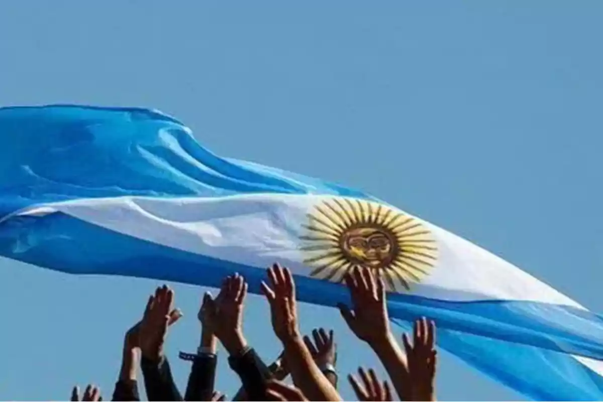 Hands raised toward an Argentine flag waving in the blue sky Hands raised toward an Argentine flag waving in the blue sky