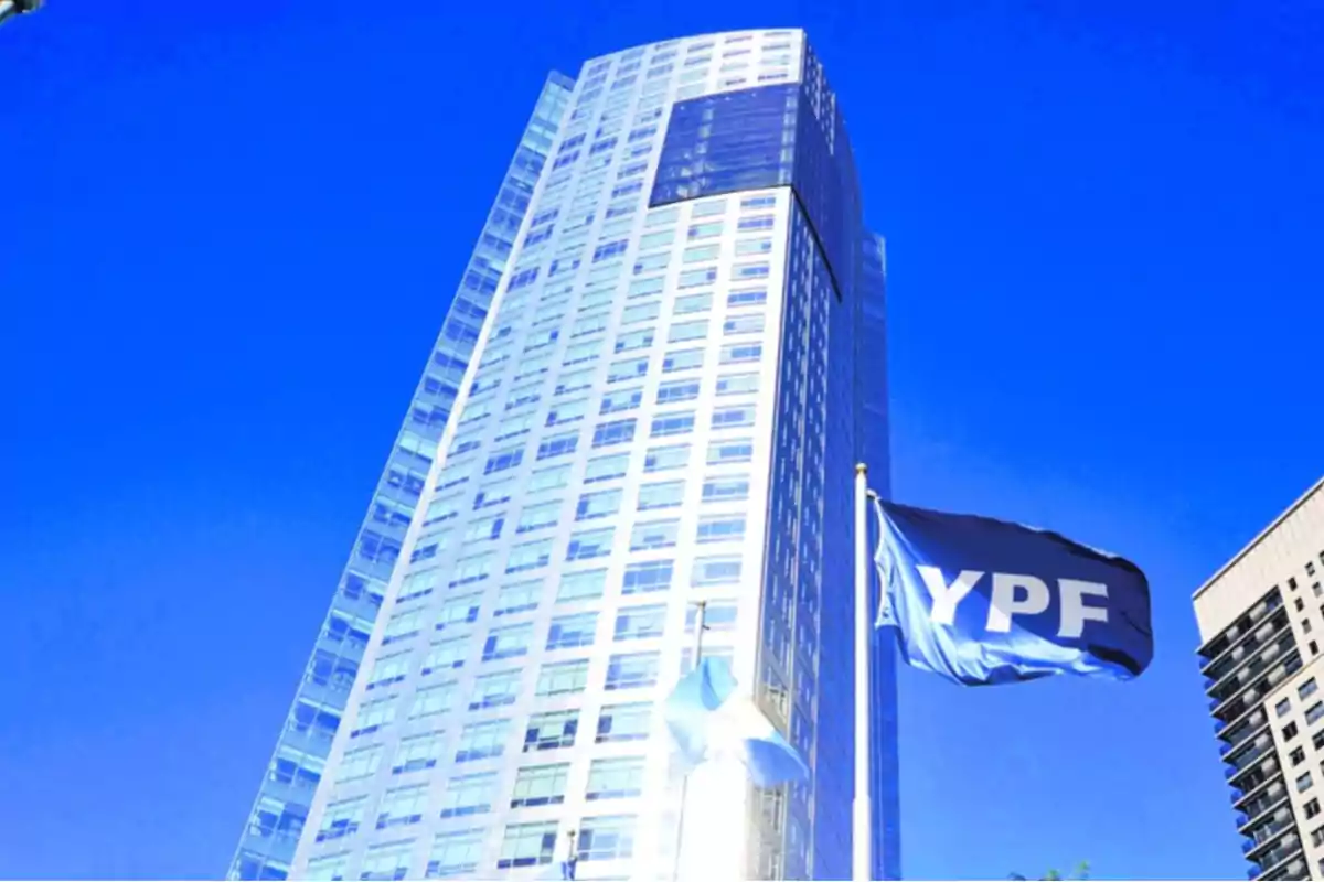 Edificio moderno de gran altura con una bandera de YPF ondeando en primer plano bajo un cielo azul intenso