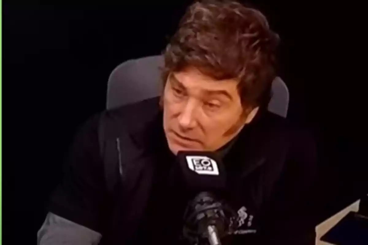 Hombre de cabello castaño hablando frente a un micrófono en un estudio de radio