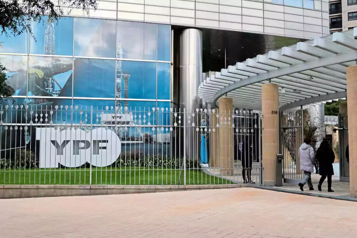 Fachada de un edificio moderno de YPF con un cartel grande y personas entrando por la puerta principal Fachada de un edificio moderno de YPF con un cartel grande y personas entrando por la puerta principal
