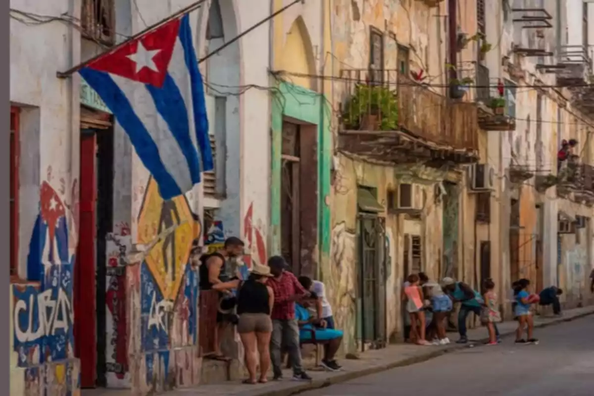 People are talking and children are playing on a street with old buildings and a Cuban flag waving on the facade. People are talking and children are playing on a street with old buildings and a Cuban flag waving on the facade.