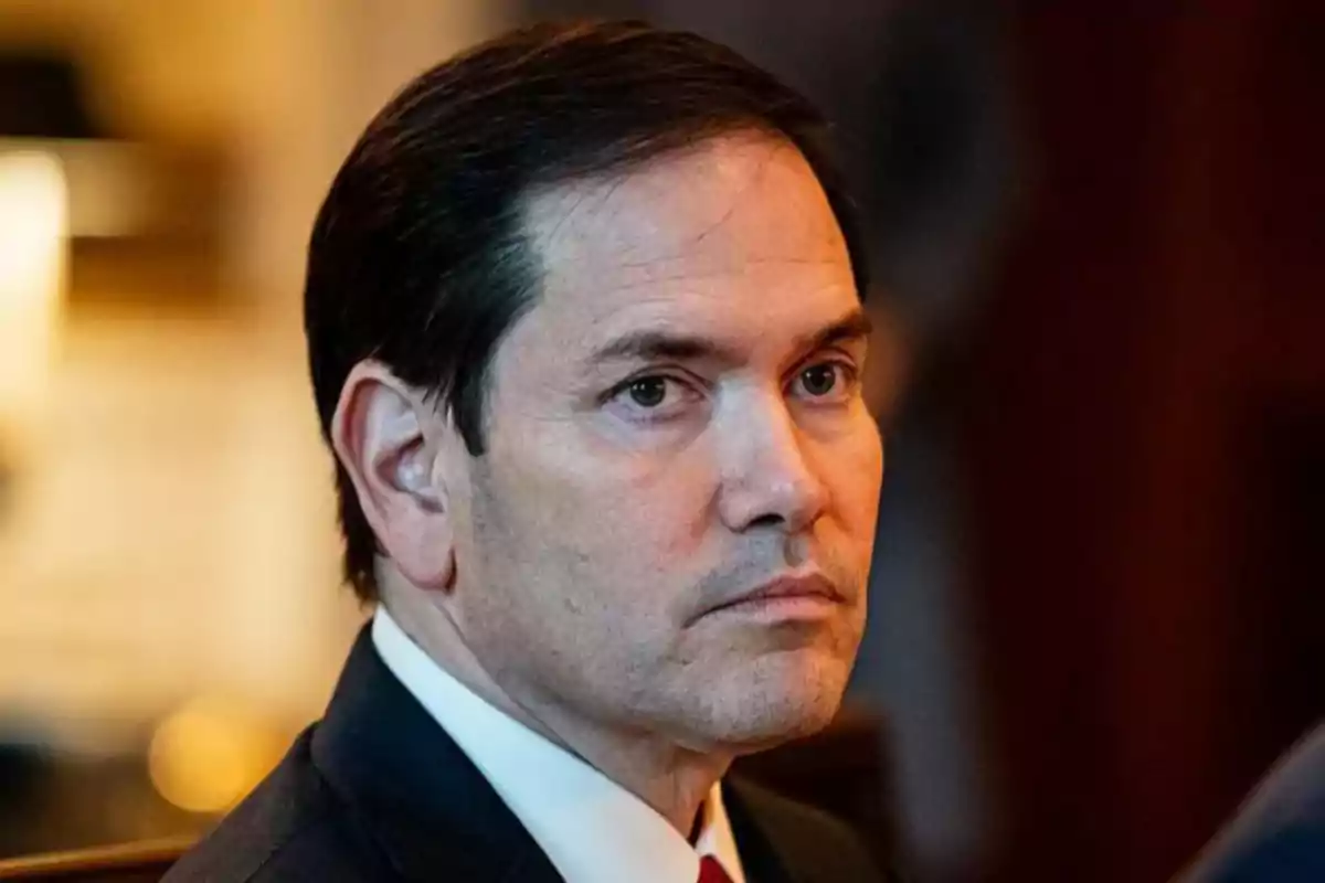 Dark-haired man with a serious expression wearing a suit and tie in a well-lit indoor setting. Dark-haired man with a serious expression wearing a suit and tie in a well-lit indoor setting.