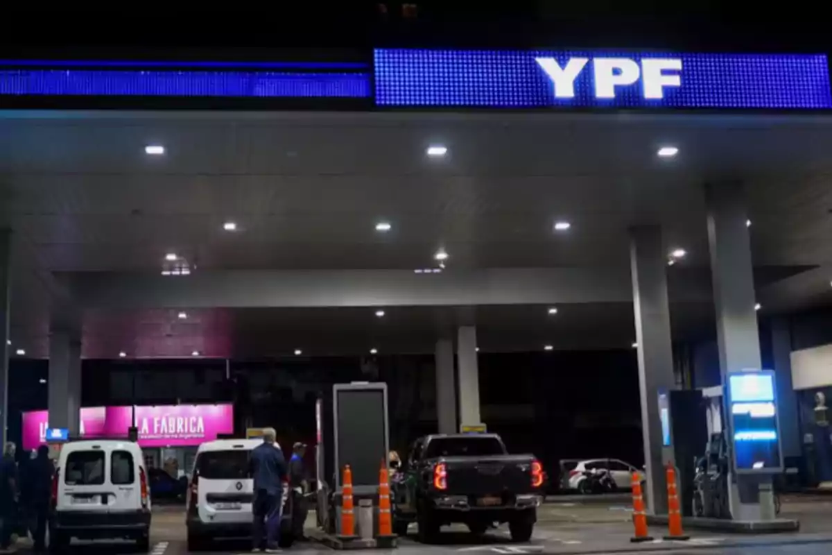 Estación de servicio YPF de noche con varios autos cargando combustible y personas alrededor
