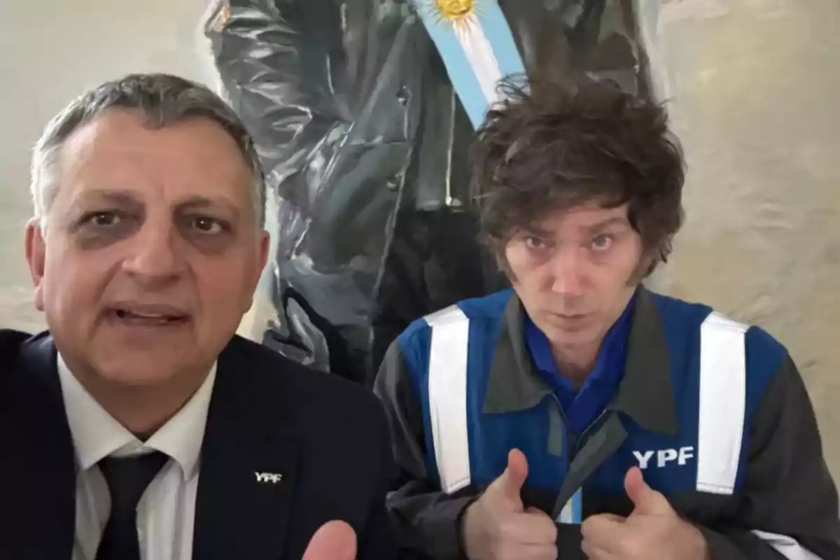 Dos hombres posan para una selfie, ambos llevan ropa con el logo de YPF y uno de ellos hace el gesto de pulgares arriba, al fondo se ve una pintura con una banda celeste y blanca. Dos hombres posan para una selfie, ambos llevan ropa con el logo de YPF y uno de ellos hace el gesto de pulgares arriba, al fondo se ve una pintura con una banda celeste y blanca.