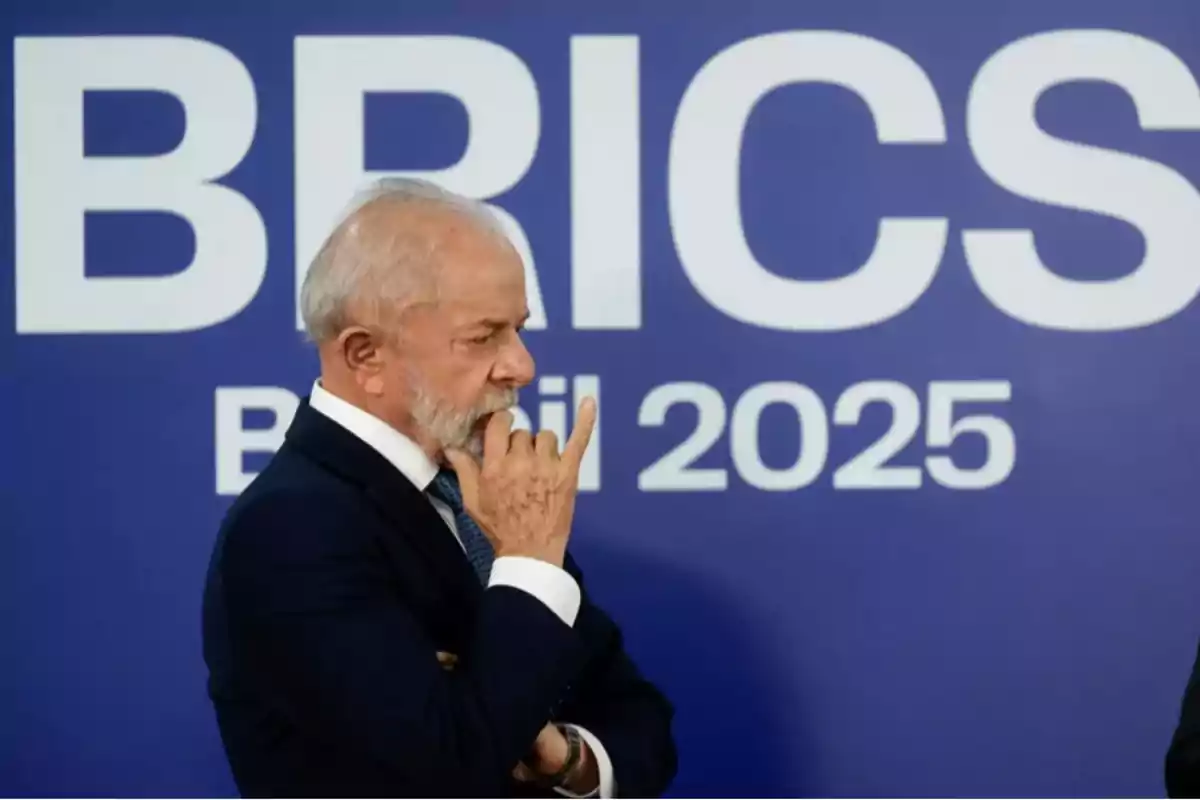 Gray-haired, bearded man dressed in a dark suit in a thoughtful pose in front of a blue sign with the words BRICS Brazil 2025. Gray-haired, bearded man dressed in a dark suit in a thoughtful pose in front of a blue sign with the words BRICS Brazil 2025.