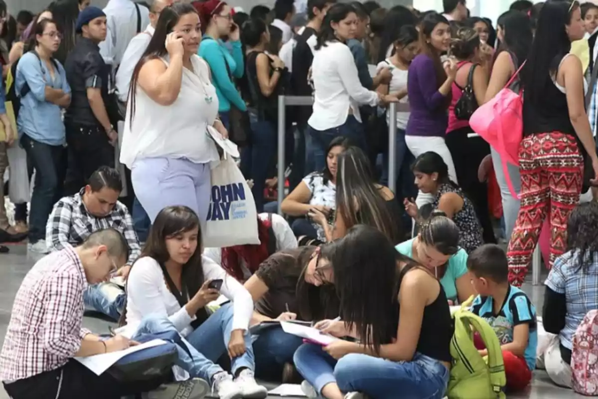Group of young people sitting and standing in an indoor space, some writing or using their cell phones, while waiting their turn in a crowded line. Group of young people sitting and standing in an indoor space, some writing or using their cell phones, while waiting their turn in a crowded line.