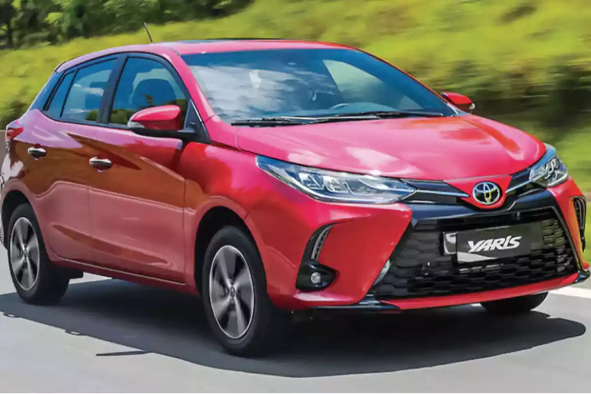 Auto compacto Toyota Yaris color rojo circulando por una carretera rodeada de vegetación Auto compacto Toyota Yaris color rojo circulando por una carretera rodeada de vegetación