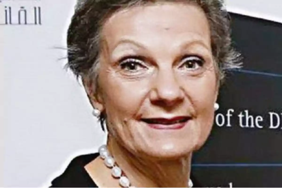 Mujer de cabello corto y canoso con collar de perlas y fondo con texto en inglés. Mujer de cabello corto y canoso con collar de perlas y fondo con texto en inglés.