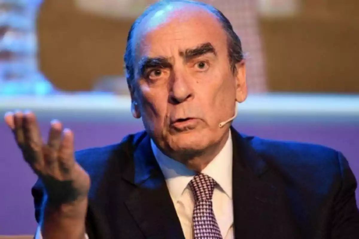 Man in a suit and tie speaking at an event with a microphone on his cheek and a serious expression Man in a suit and tie speaking at an event with a microphone on his cheek and a serious expression
