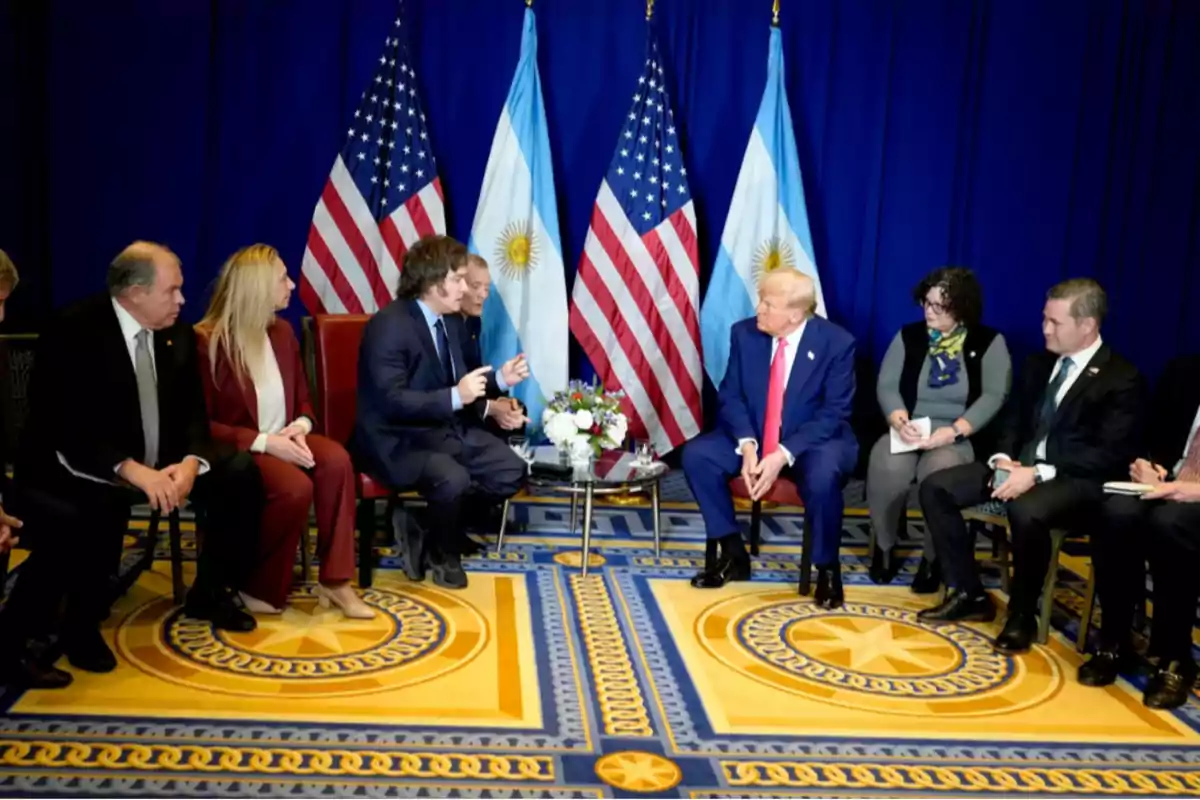 Several people sitting in a circle are talking in a room with United States and Argentine flags in the background. Several people sitting in a circle are talking in a room with United States and Argentine flags in the background.
