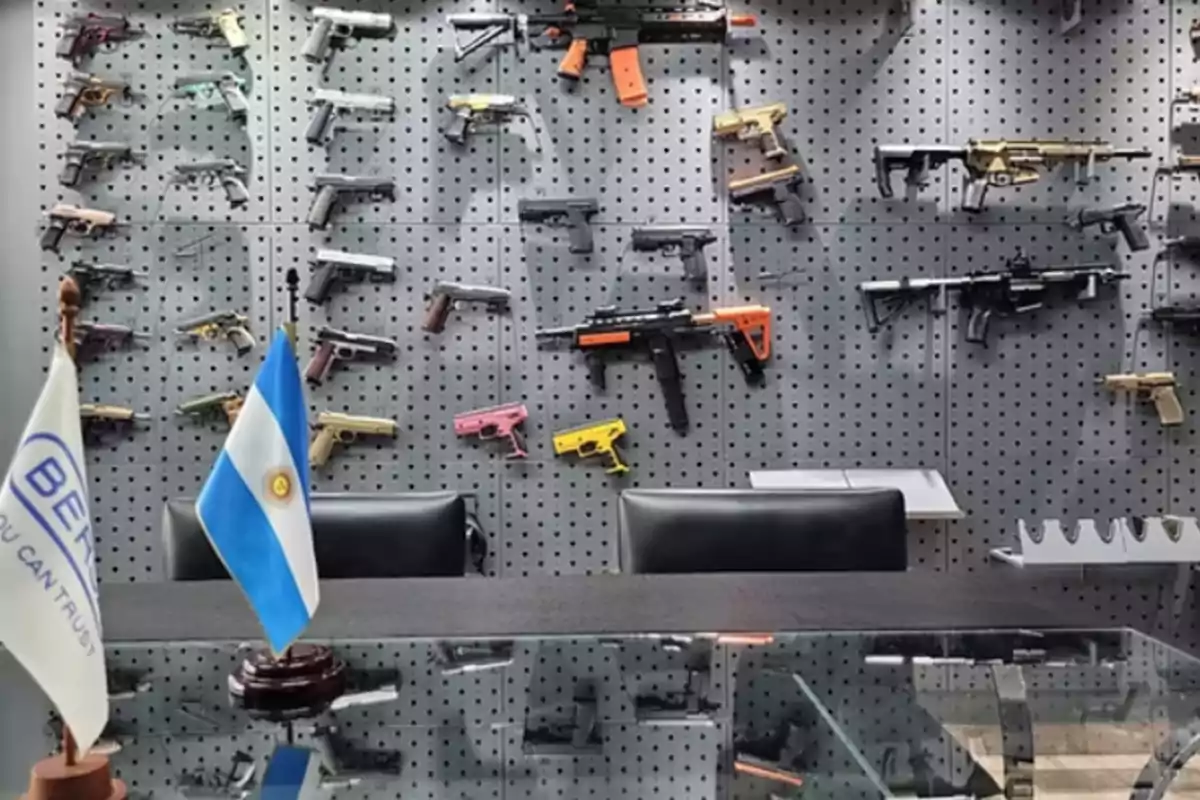 Wall with several firearms displayed behind a desk with two flags, one of them from Argentina