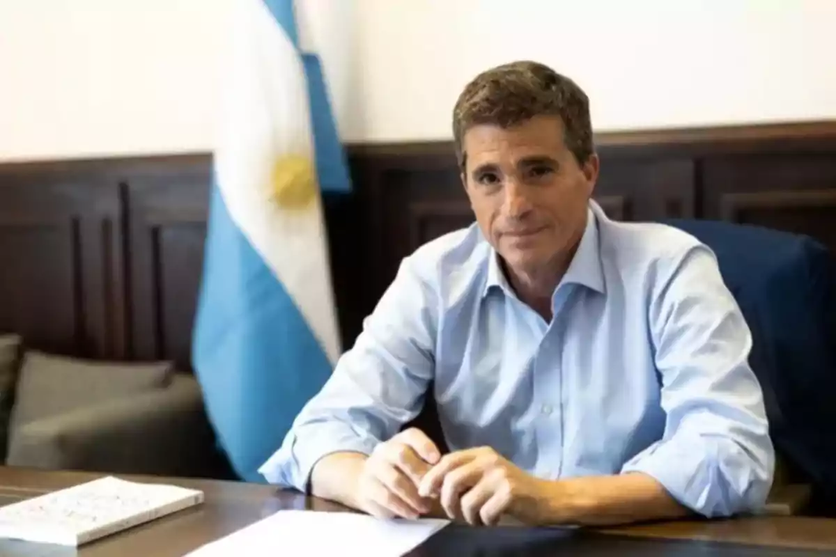 Short-haired, gray-haired man sitting at a desk with an Argentine flag in the background Short-haired, gray-haired man sitting at a desk with an Argentine flag in the background