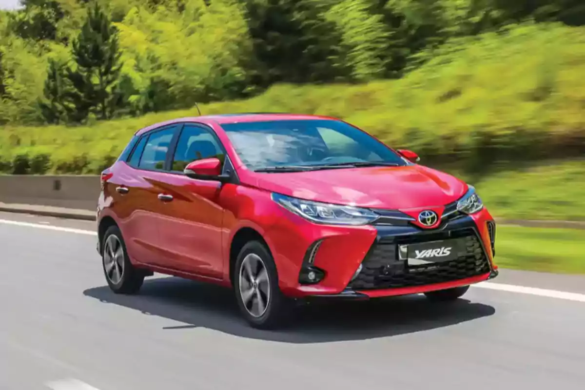 Red compact Toyota Yaris driving on a road surrounded by vegetation Red compact Toyota Yaris driving on a road surrounded by vegetation