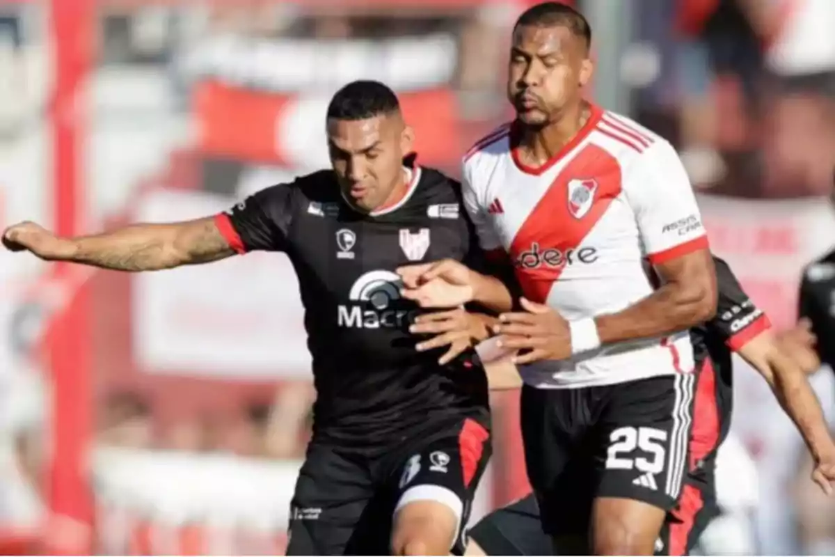 Two players compete for the ball during a match, one wearing a black uniform and the other wearing a white uniform with a diagonal red stripe. Two players compete for the ball during a match, one wearing a black uniform and the other wearing a white uniform with a diagonal red stripe.