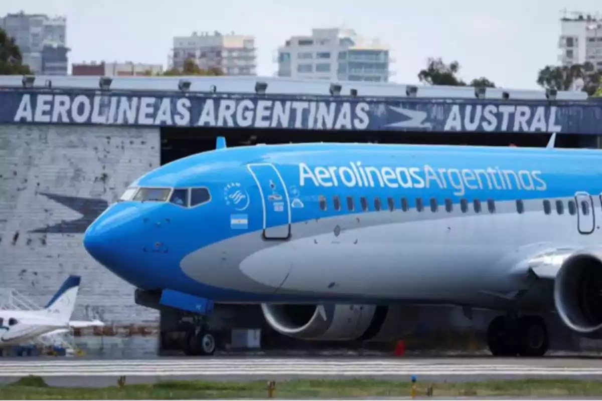 Avión de Aerolíneas Argentinas en pista frente a un hangar con el nombre de la compañía y edificios al fondo