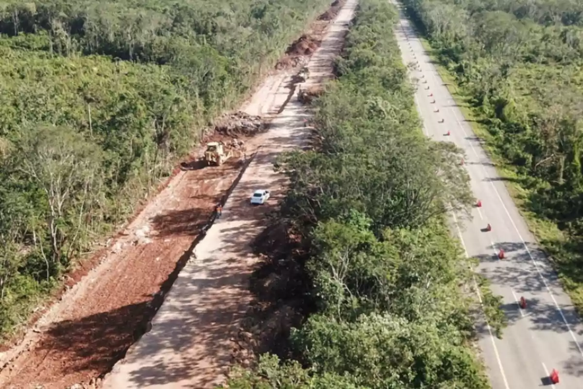 Vista aérea de una carretera en construcción junto a una vía ya existente rodeada de vegetación y árboles