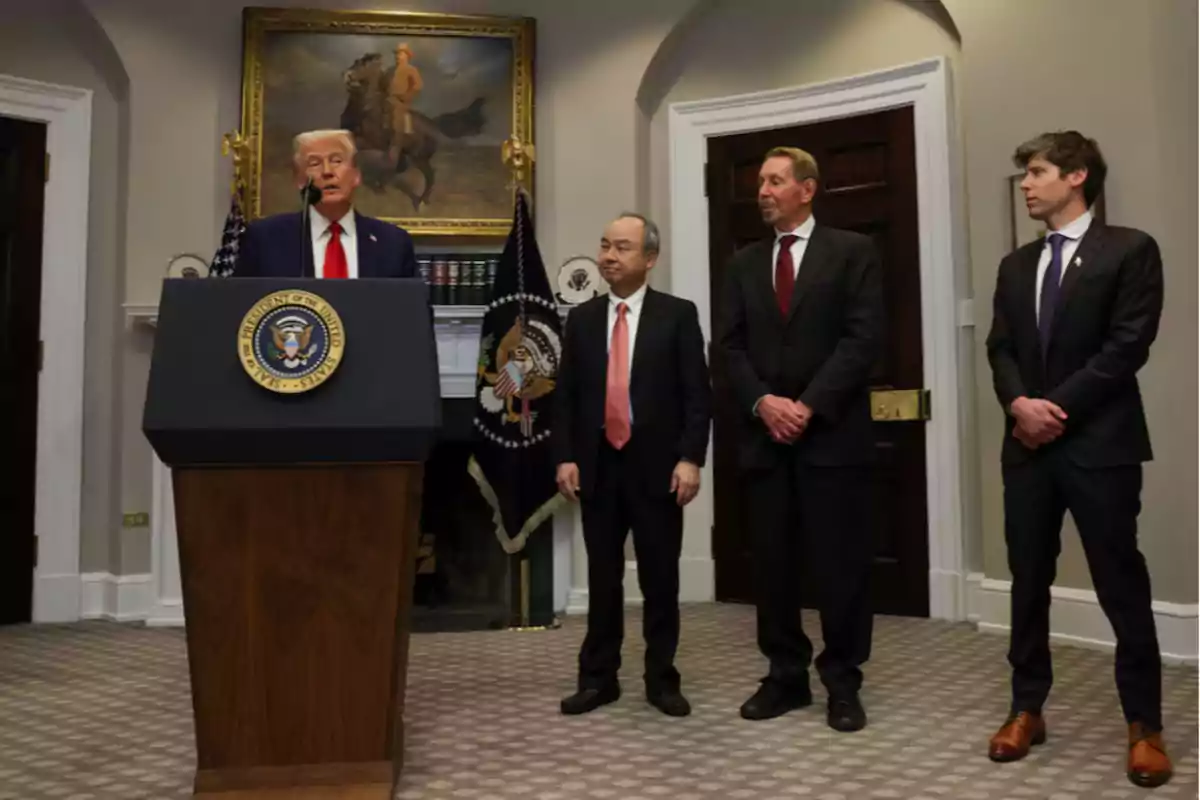 Four men in suits in an official room, one of them speaking at a presidential podium while the other three watch him.