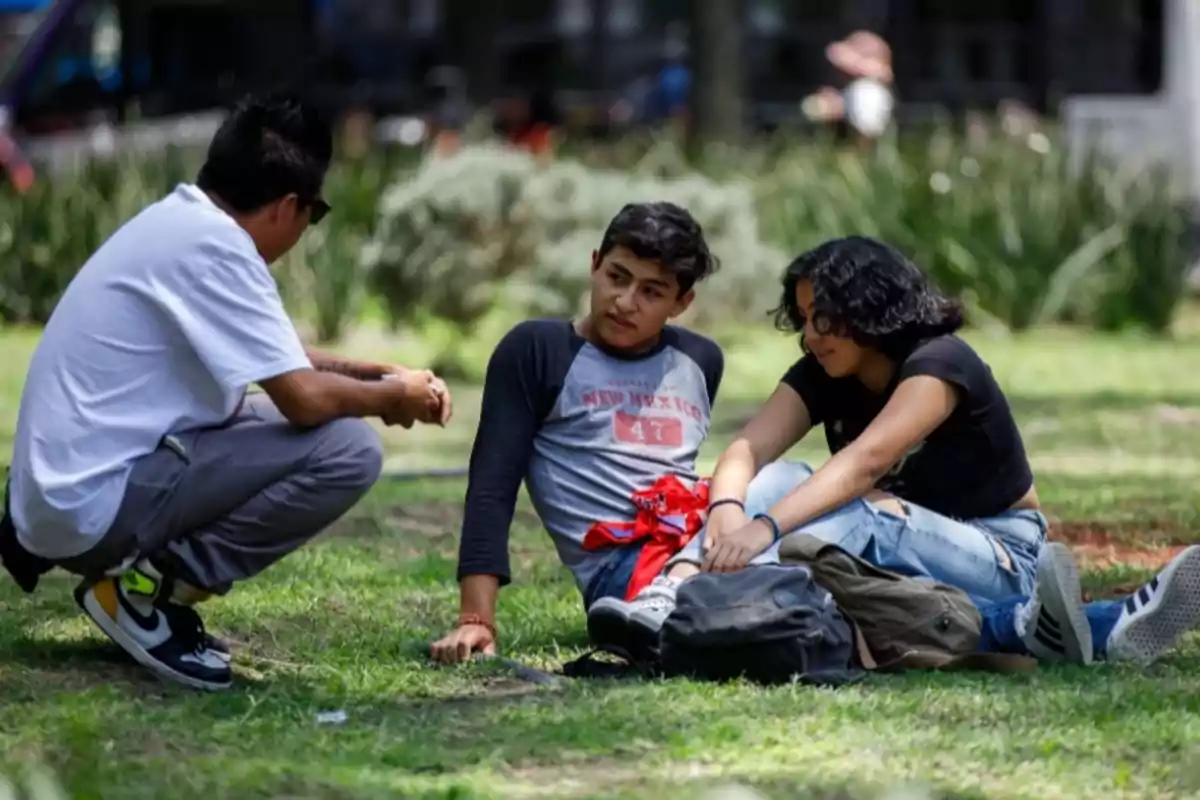 Tres jóvenes platican sentados sobre el pasto en un parque en un día soleado Tres jóvenes platican sentados sobre el pasto en un parque en un día soleado