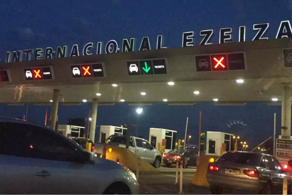Cars lining up at the entrance of Ezeiza International Airport at night, with illuminated signs indicating open and closed lanes.