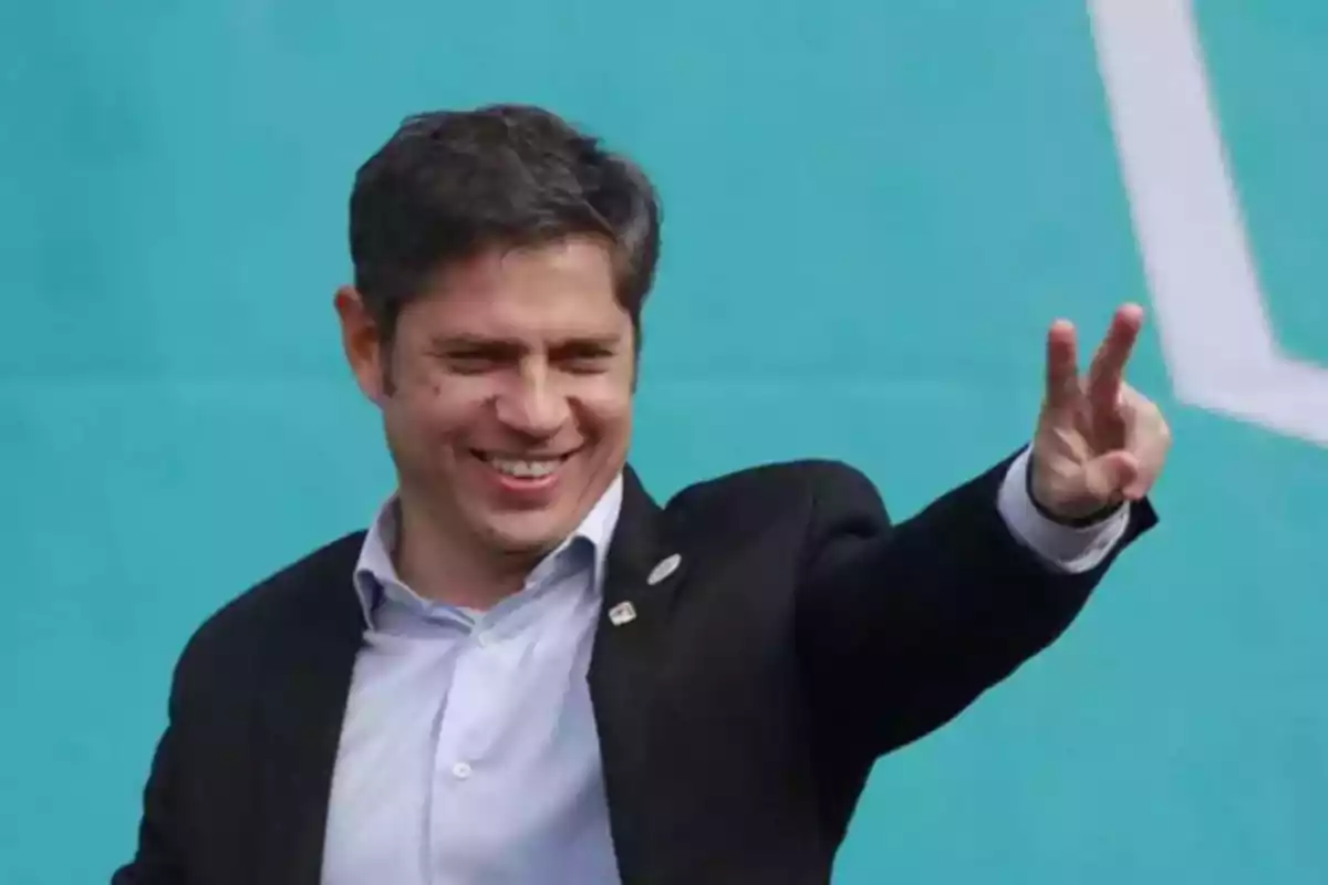 Smiling man in a dark jacket and light jersey making the victory sign with his hand in front of a light blue background Smiling man in a dark jacket and light jersey making the victory sign with his hand in front of a light blue background