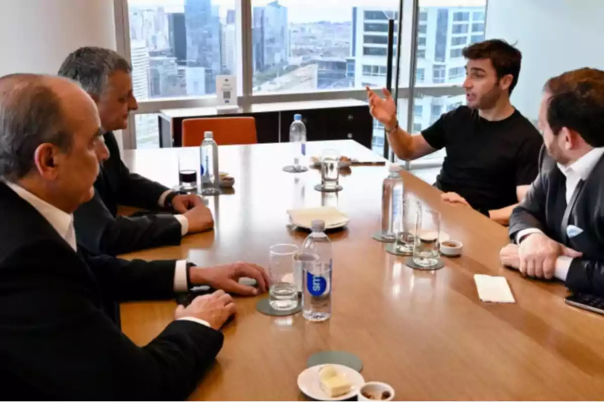 Four men sitting around a conference table talk in a modern office with large windows and a view of the city. Four men sitting around a conference table talk in a modern office with large windows and a view of the city.