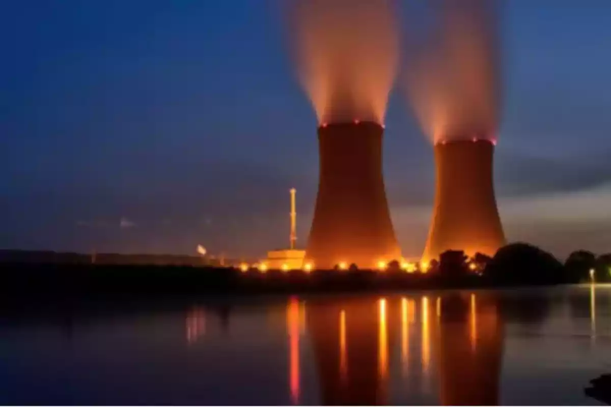 Cooling towers of a nuclear plant illuminated at dusk with steam rising into the sky and their reflection in the water.