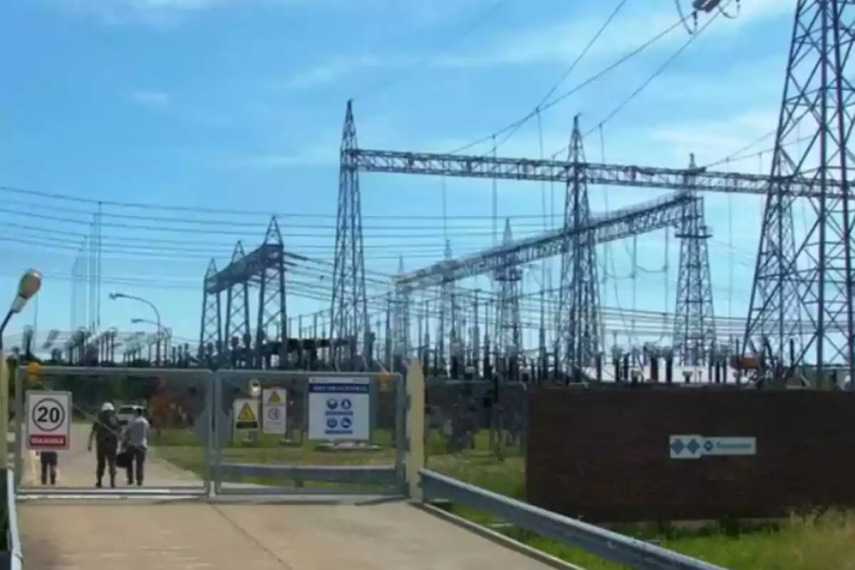 Personas ingresando a una subestación eléctrica rodeada de torres y cables de alta tensión en un día soleado