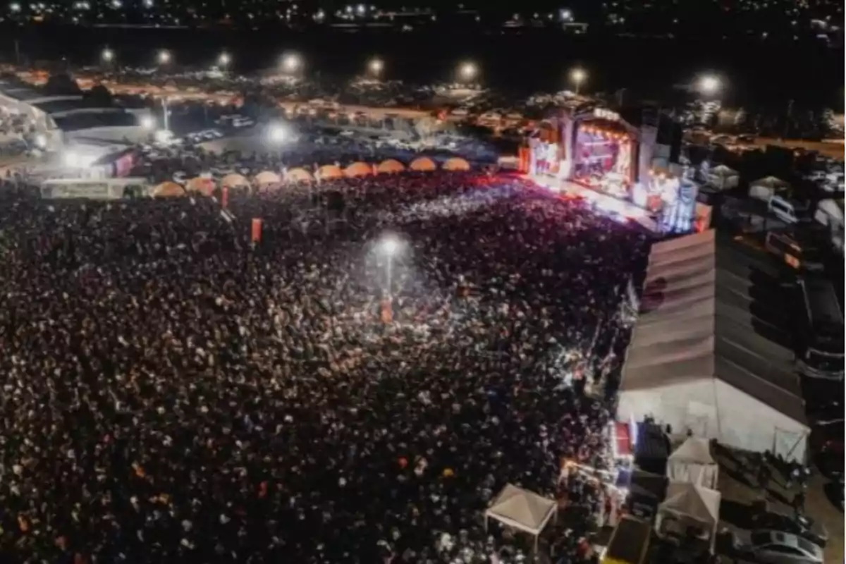 Vista aérea de un multitudinario concierto al aire libre durante la noche con luces brillantes y un escenario iluminado Vista aérea de un multitudinario concierto al aire libre durante la noche con luces brillantes y un escenario iluminado