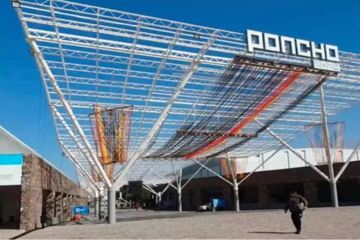 Estructura metálica moderna con el letrero Poncho 2024 y decoraciones de hilos de colores bajo un cielo azul Estructura metálica moderna con el letrero Poncho 2024 y decoraciones de hilos de colores bajo un cielo azul
