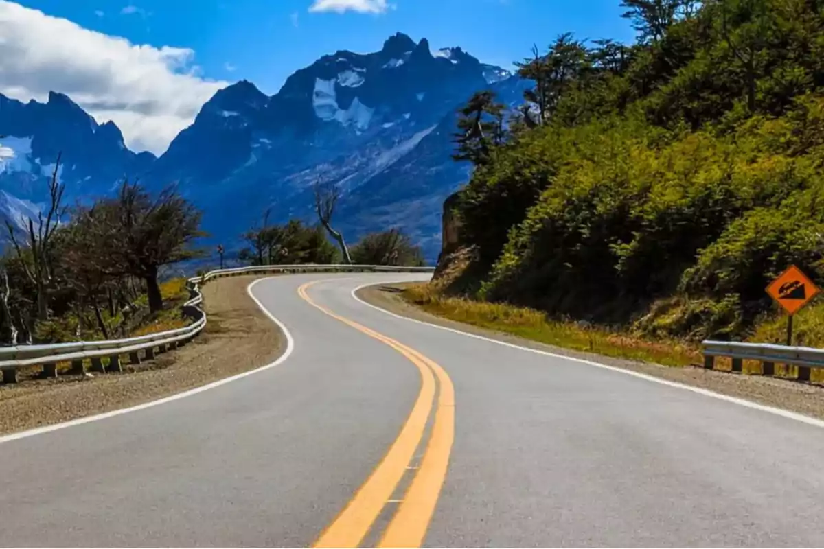 Carretera asfaltada con curvas rodeada de vegetación y montañas al fondo bajo un cielo azul